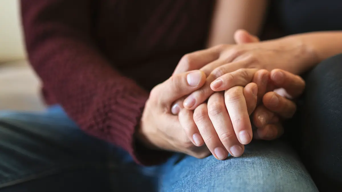 Dos personas se sostienen las manos como gesto de apoyo emocional